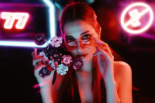 নিয়ন আলোয় আলোকিত পরিবেশে ক্যাসিনো চিপ হাতে এক অভিজাত নারী—যা BK33B–এর প্রিমিয়াম অনলাইন ক্যাসিনো পরিবেশকে তুলে ধরে।